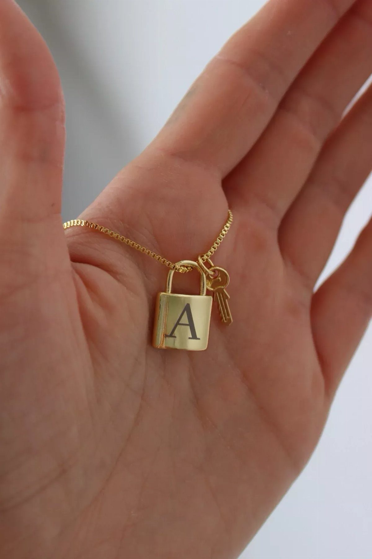 Gold padlock necklace engraved with letter A and a small gold key charm