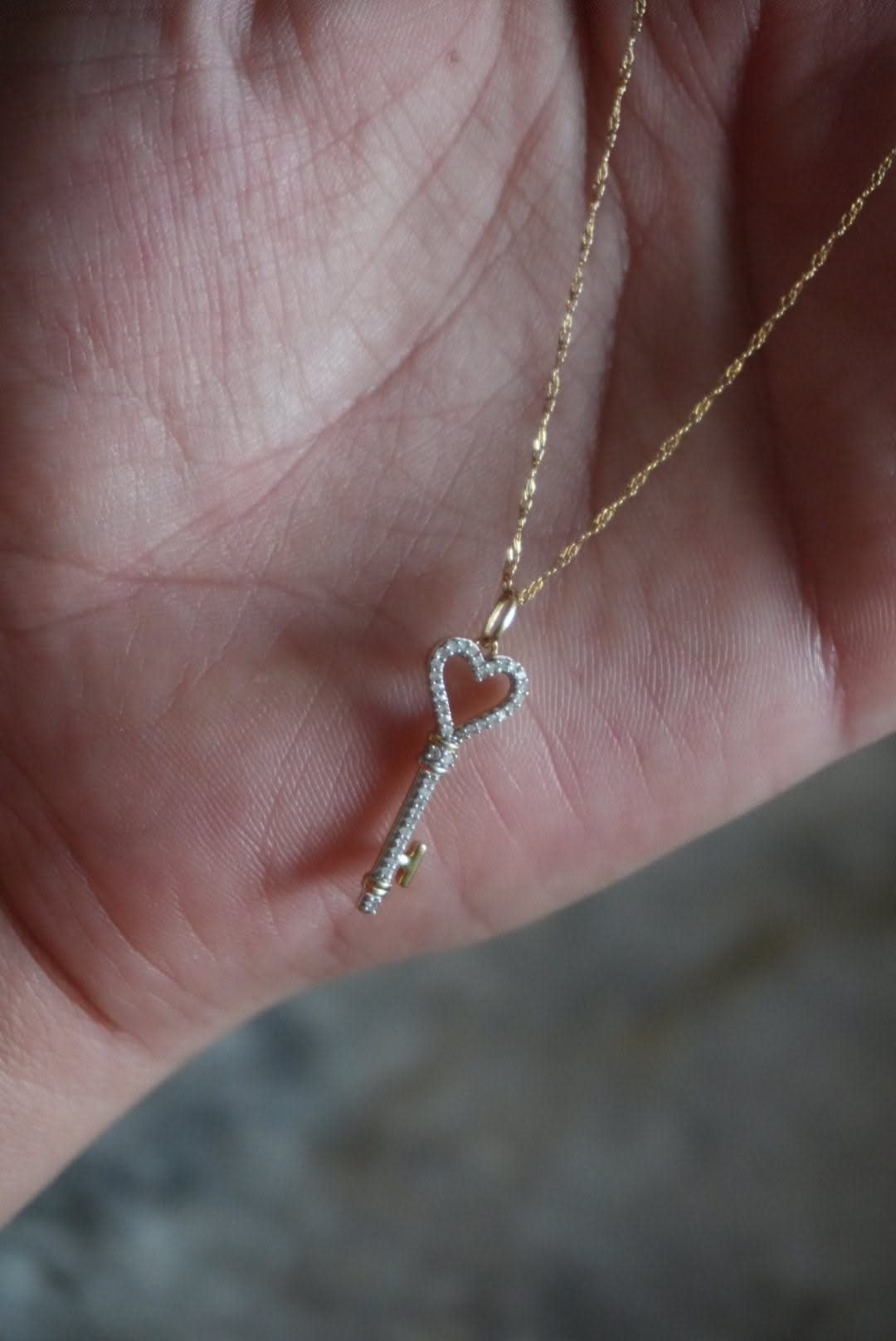 Gold key pendant with a diamond heart head resting on a palm