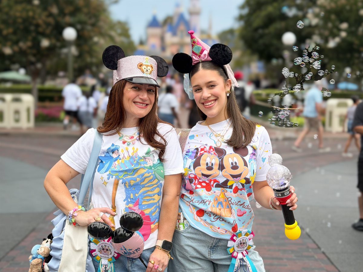 Two women wearing Disney birthday shirts and Mickey ears posing in front of the castle.