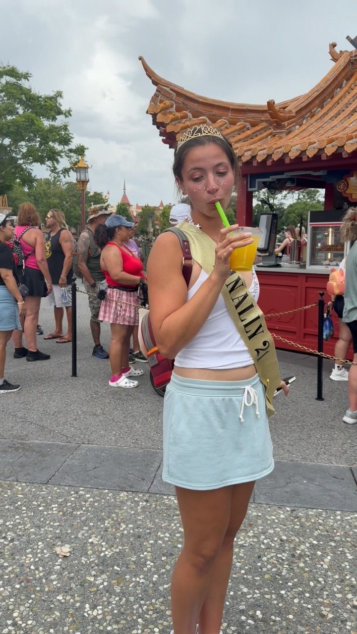 Young woman in birthday sash drinking a yellow beverage at EPCOT World Showcase.