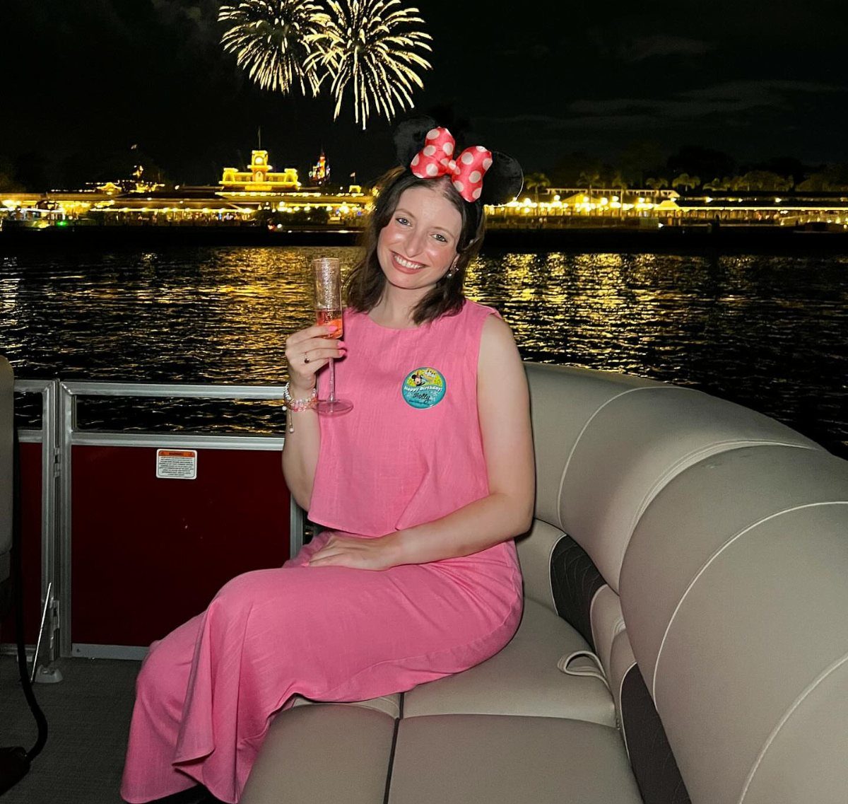 Woman in pink dress with Minnie ears watching fireworks from a boat.