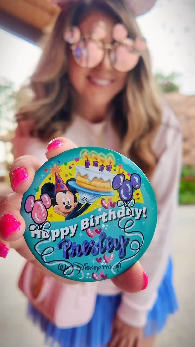 Blue Disney birthday pin with Mickey Mouse held by a person outdoors.