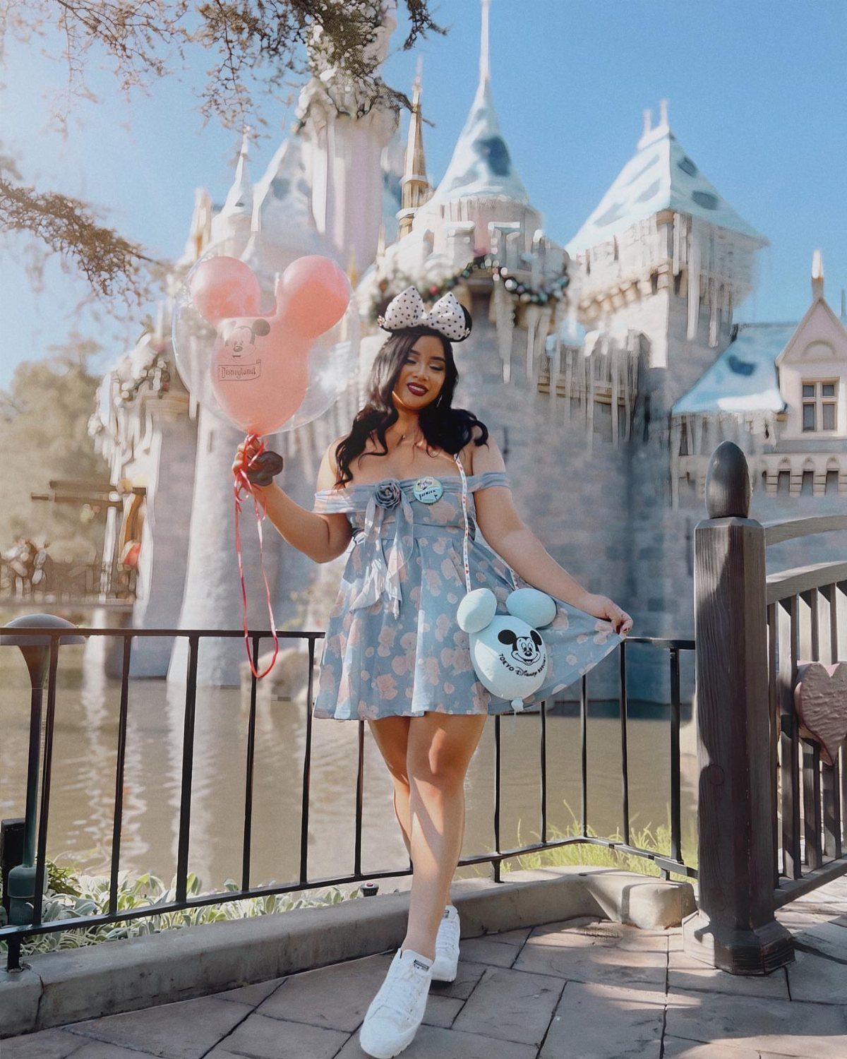 Woman in blue dress posing with Mickey balloon in front of Cinderella Castle
