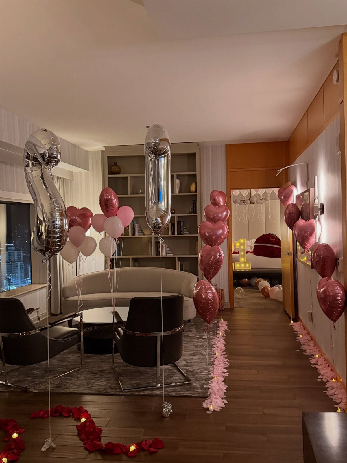Hotel room decorated with pink and silver balloons and rose petals for birthday.