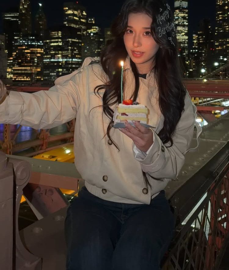 Young woman holding a birthday cake on a bridge with NYC skyline background