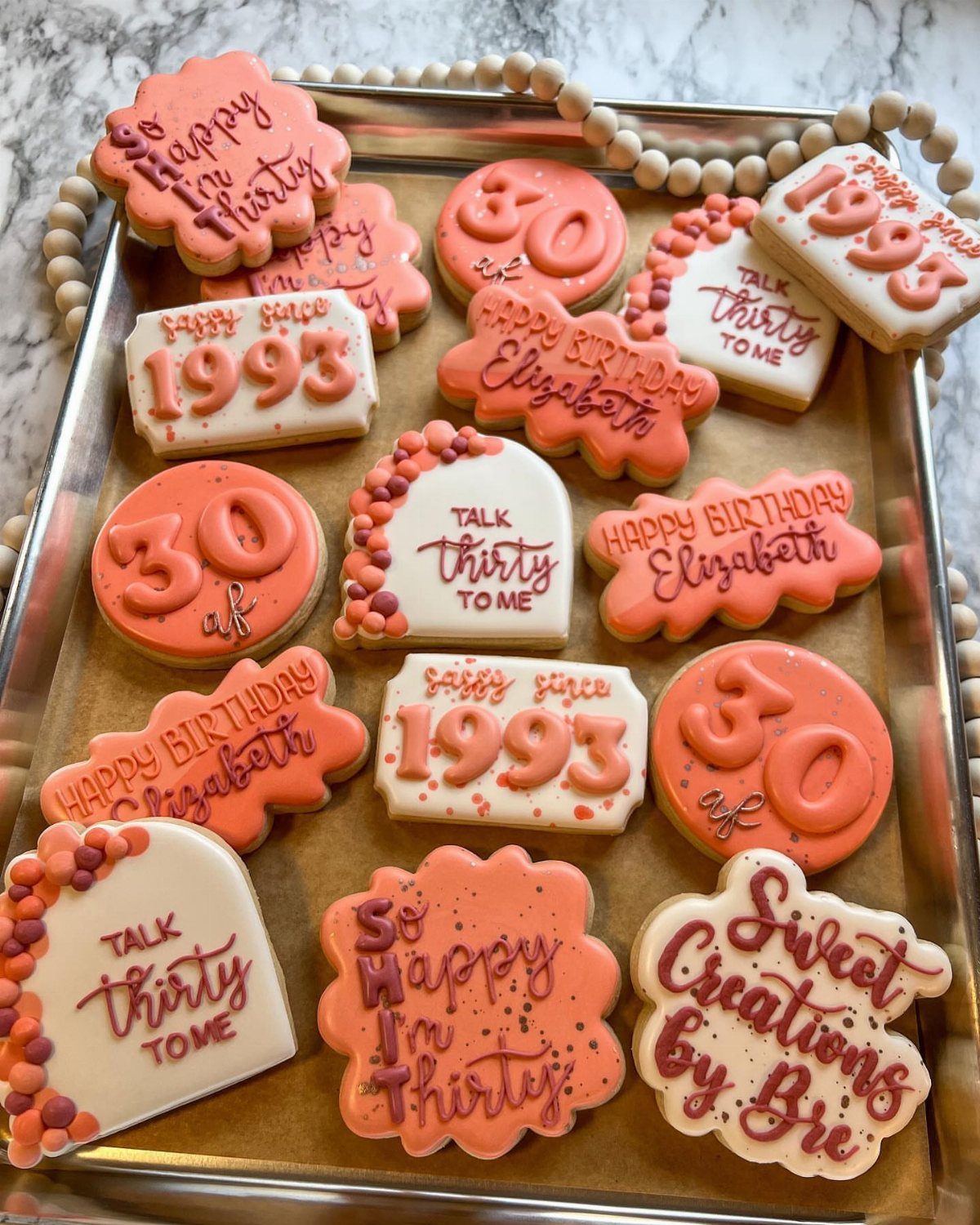 Assorted 30th birthday cookies with orange and white icing on a silver tray.