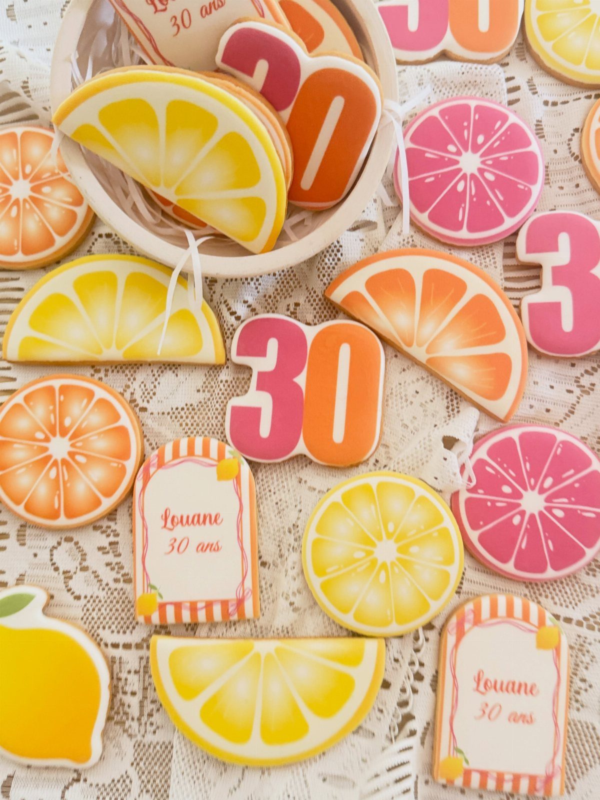 Citrus fruit shaped cookies and number 30 cookies on white lace fabric.