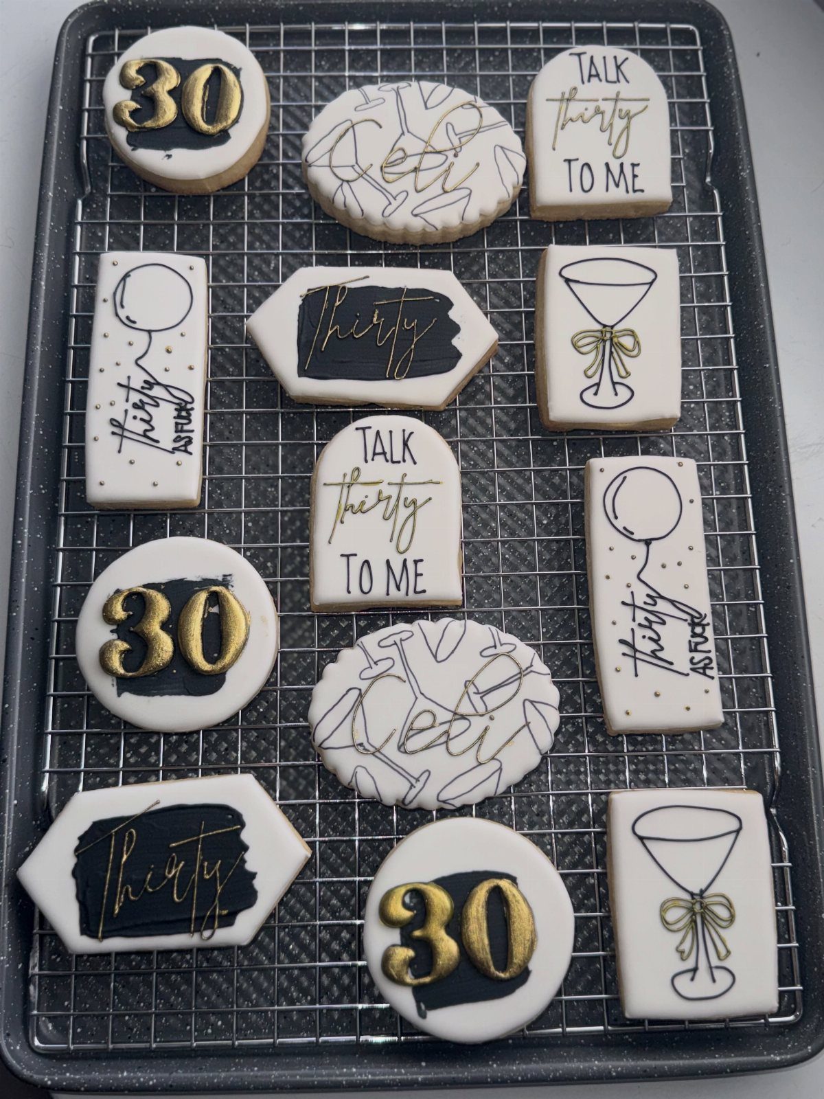 Assorted 30th birthday cookies with gold and black icing on a cooling rack.