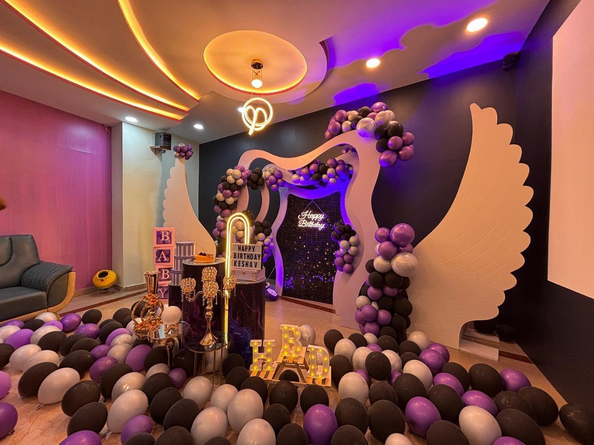 Party room decorated with purple and black balloons and large white wing cutouts.