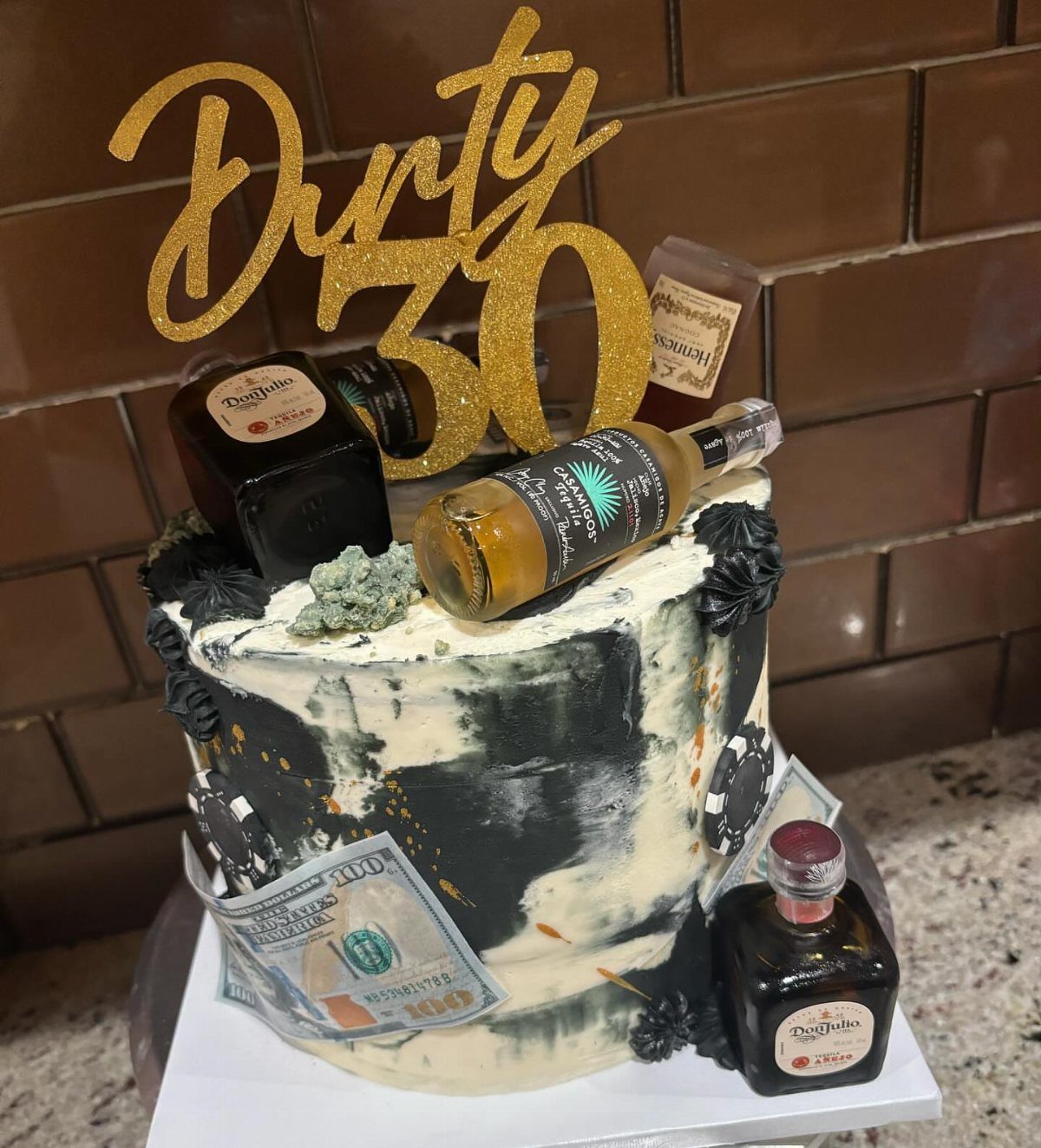 Dirty 30 cake with gold topper, miniature liquor bottles, and edible money decorations.