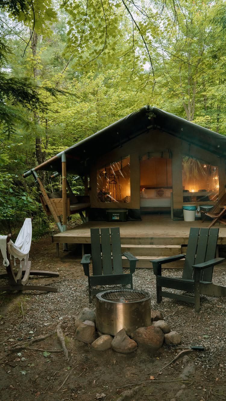 Luxury glamping tent in a forest with Adirondack chairs and a fire pit.