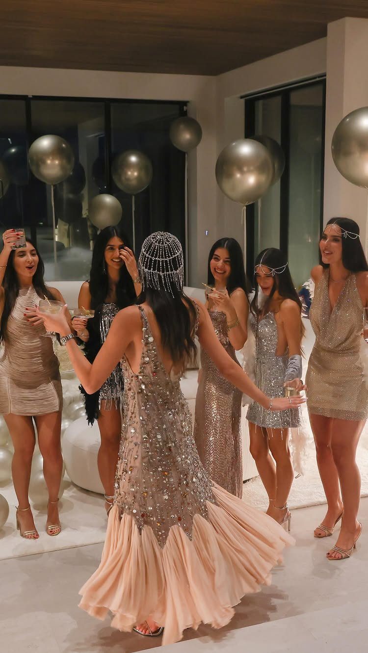 Women in 1920s flapper dresses and headbands celebrating with champagne and gold balloons.