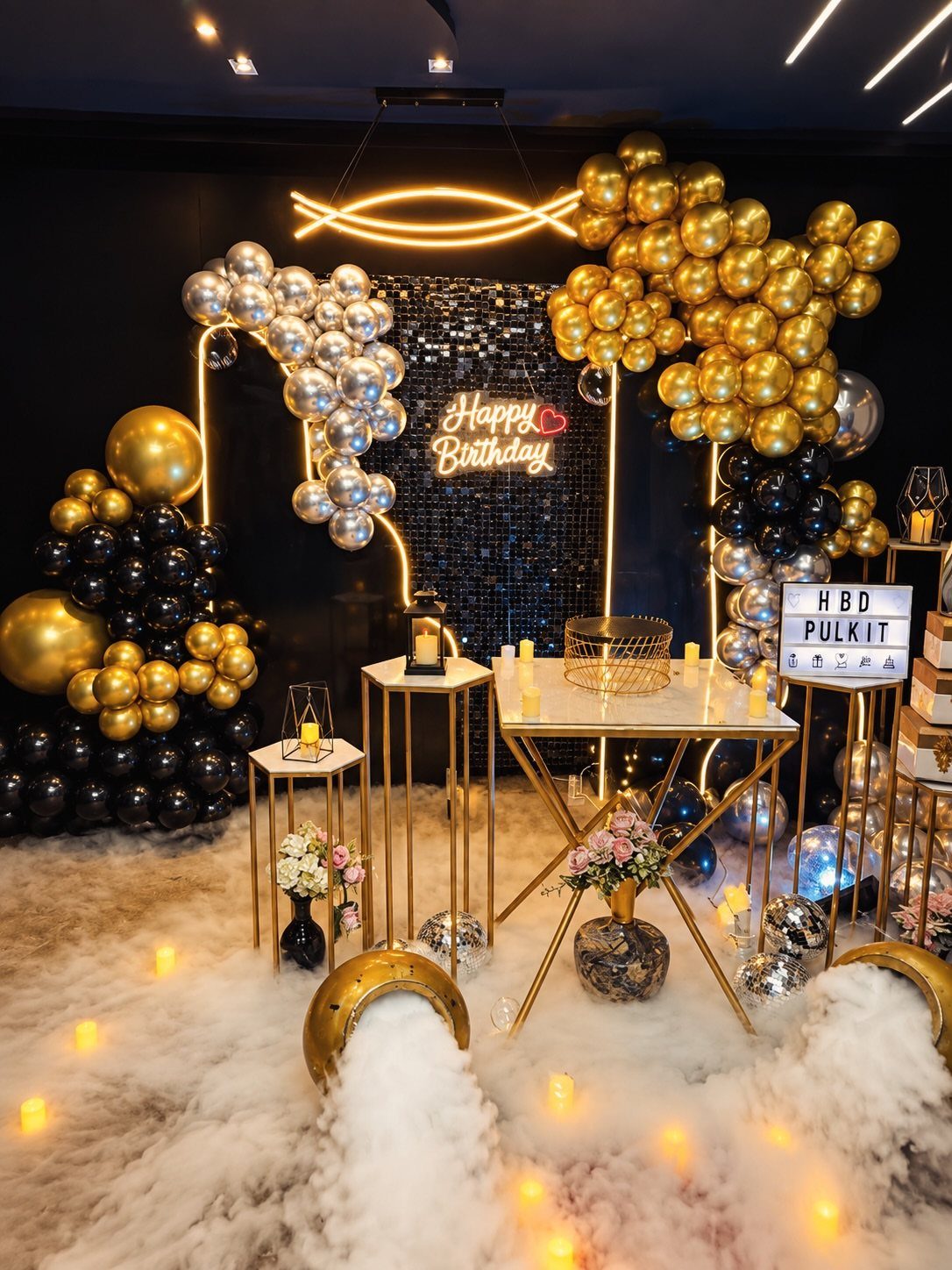 Birthday party decoration with gold and black balloons, neon sign, and fog floor.