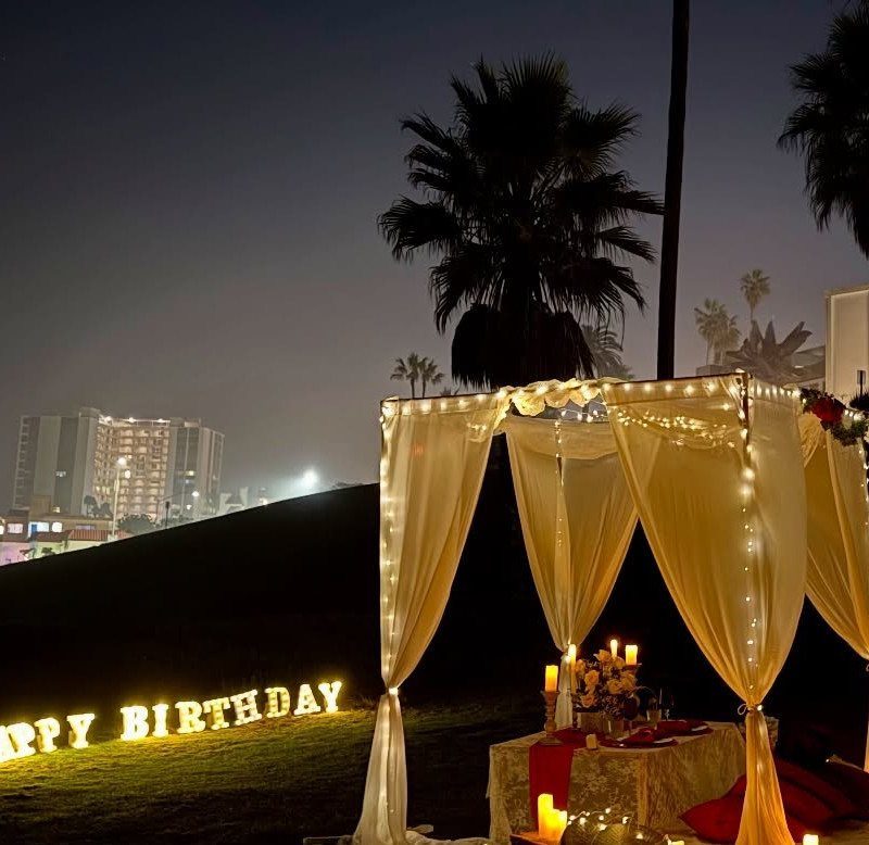 Outdoor birthday celebration setup with glowing letters, white canopy, and city skyline background