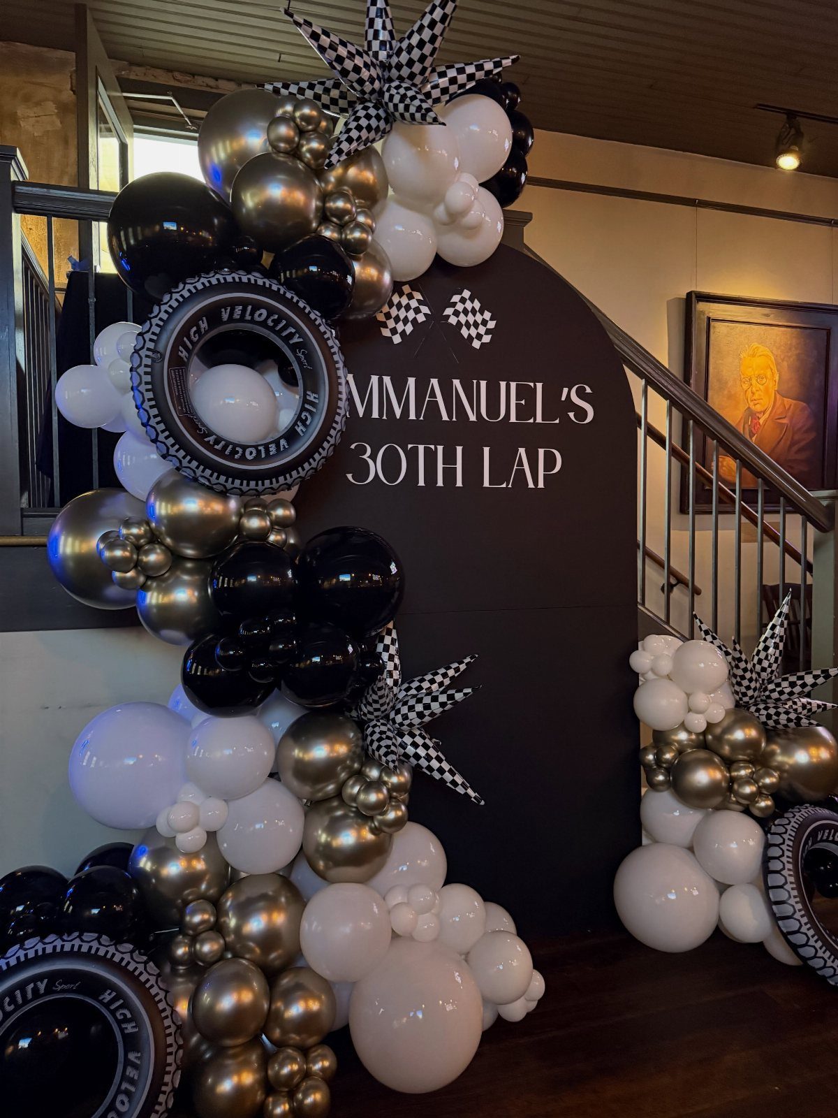 Racing themed 30th birthday backdrop with black, gold, and white balloons and tires.