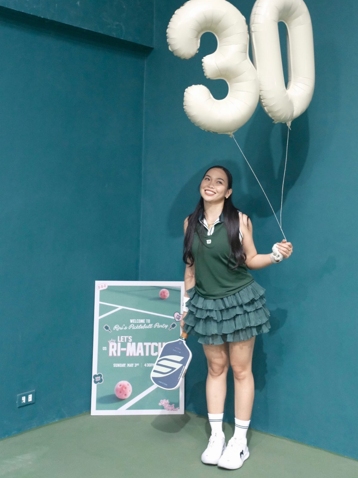 Woman in green tennis attire posing with number 30 balloons and pickleball sign.