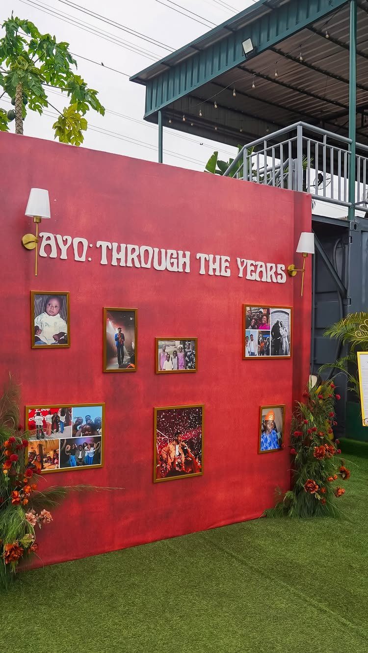 Red backdrop wall with framed photos and text celebrating a person's life milestones.