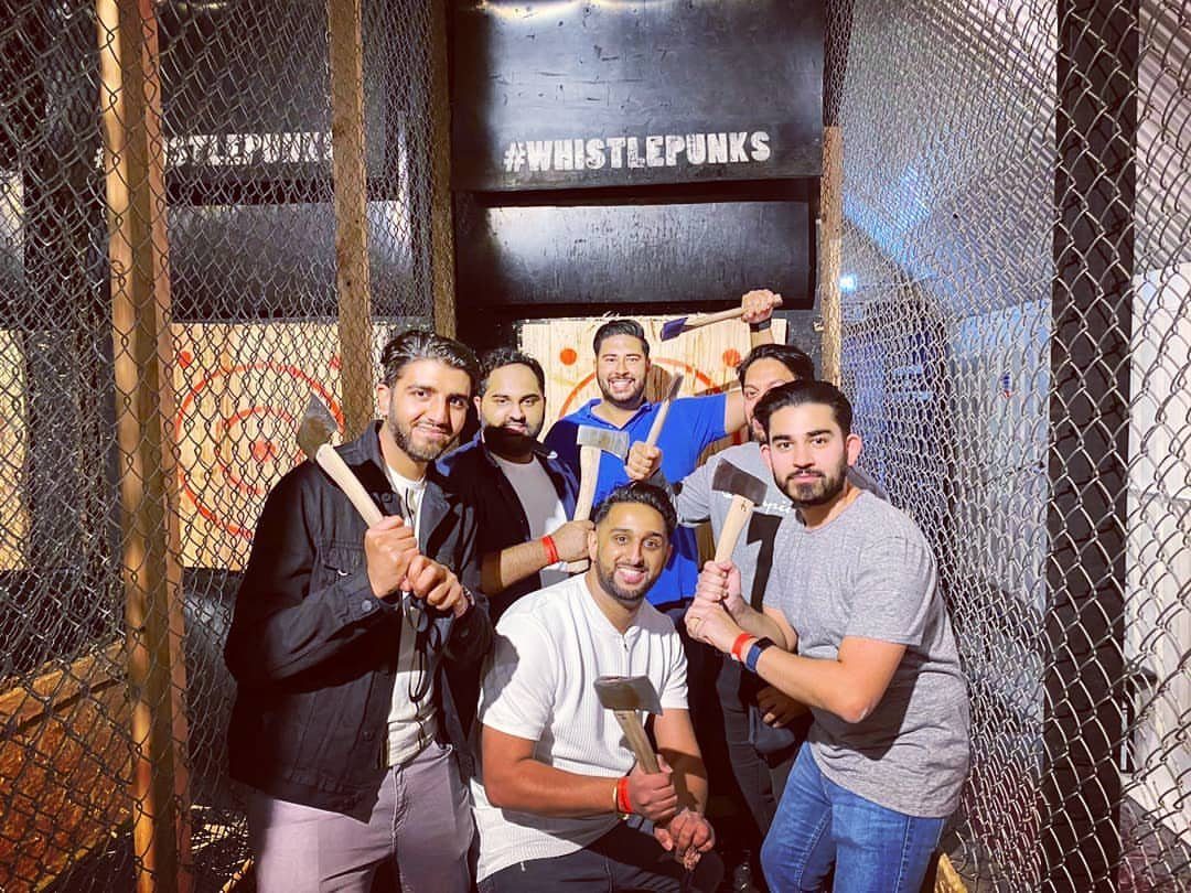 Six men posing with axes in an axe throwing lane with targets behind them.