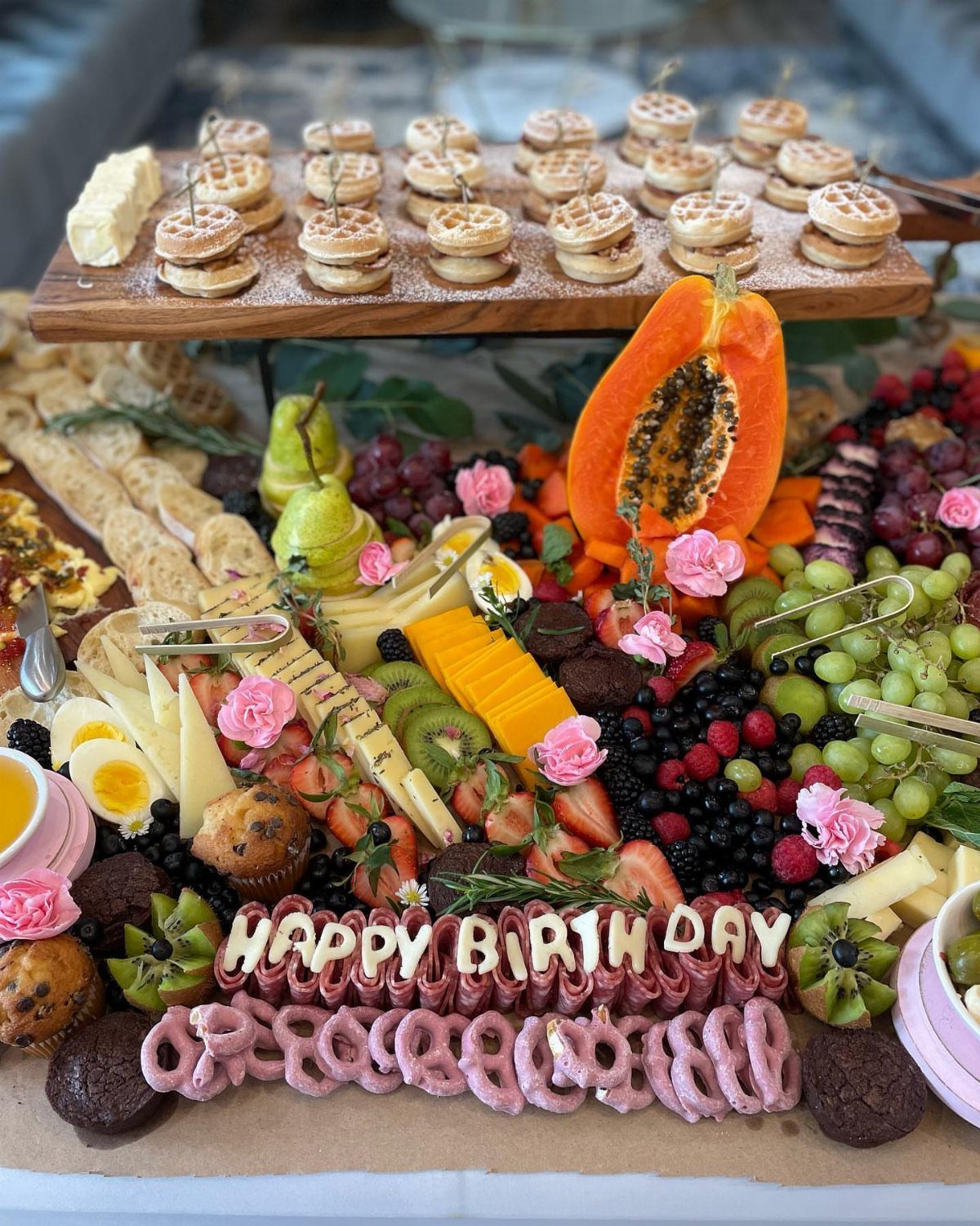 Birthday brunch grazing board with mini waffles, fresh fruit, cheeses, and meat lettering.