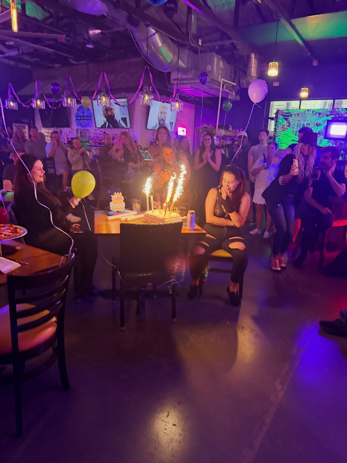 Woman sitting at a bar table with a birthday cake and sparklers.