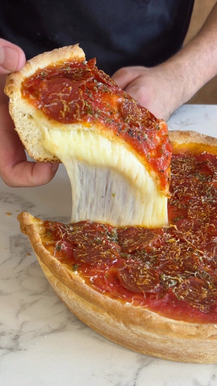 Deep dish pizza slice being lifted with stretching melted cheese on marble surface