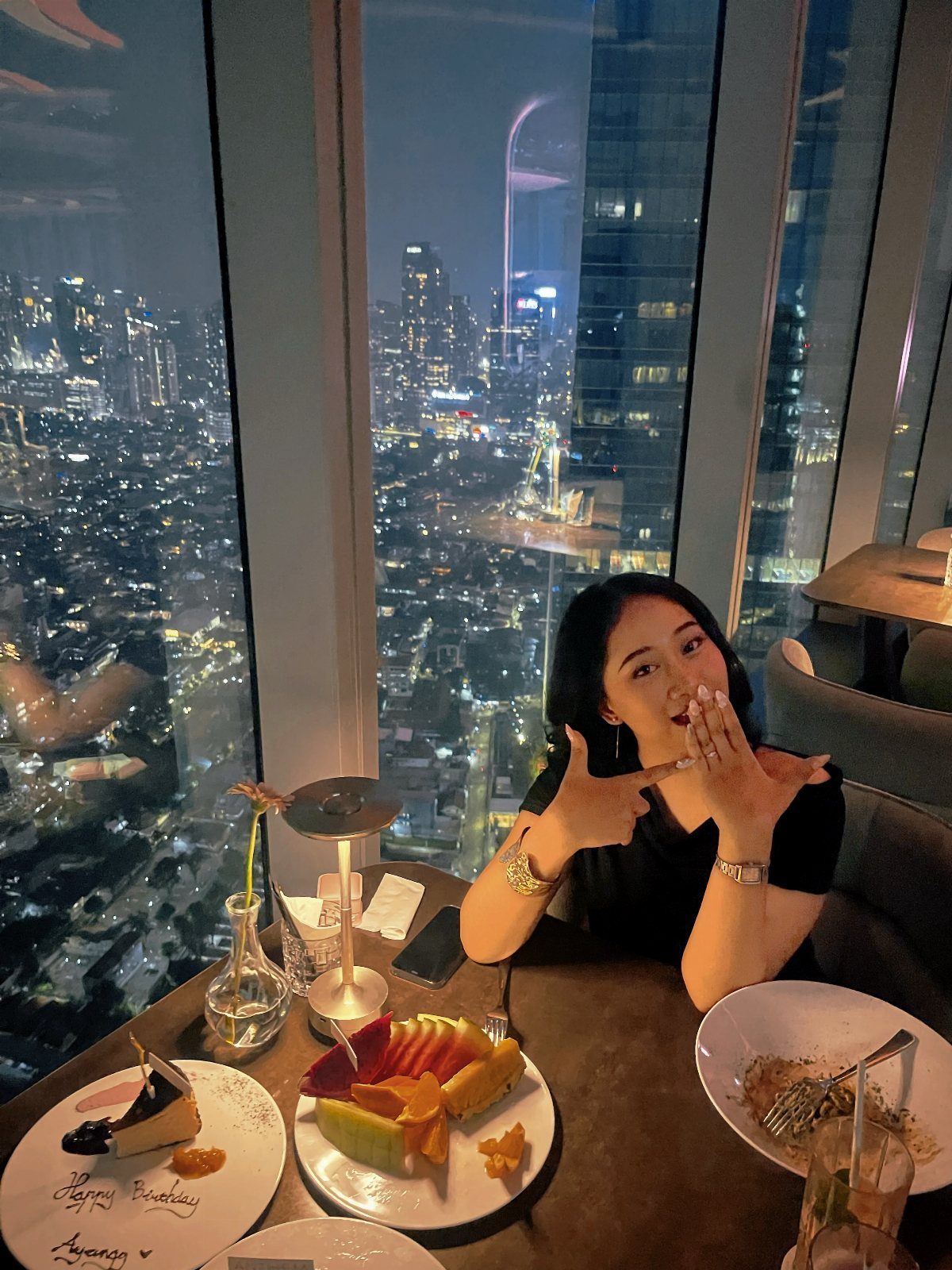 Woman dining at a high-rise restaurant with a night city skyline view.