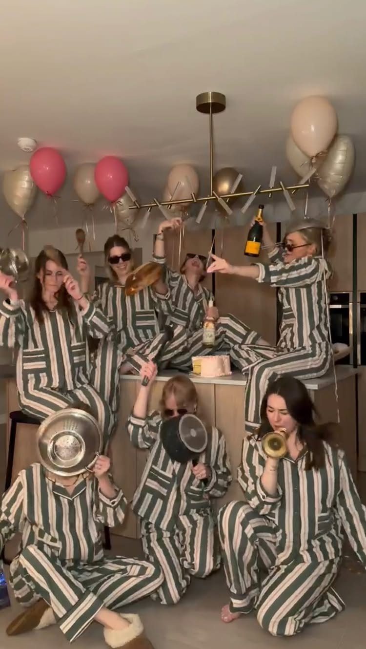 Group of women in matching striped pajamas celebrating with champagne and balloons in a kitchen