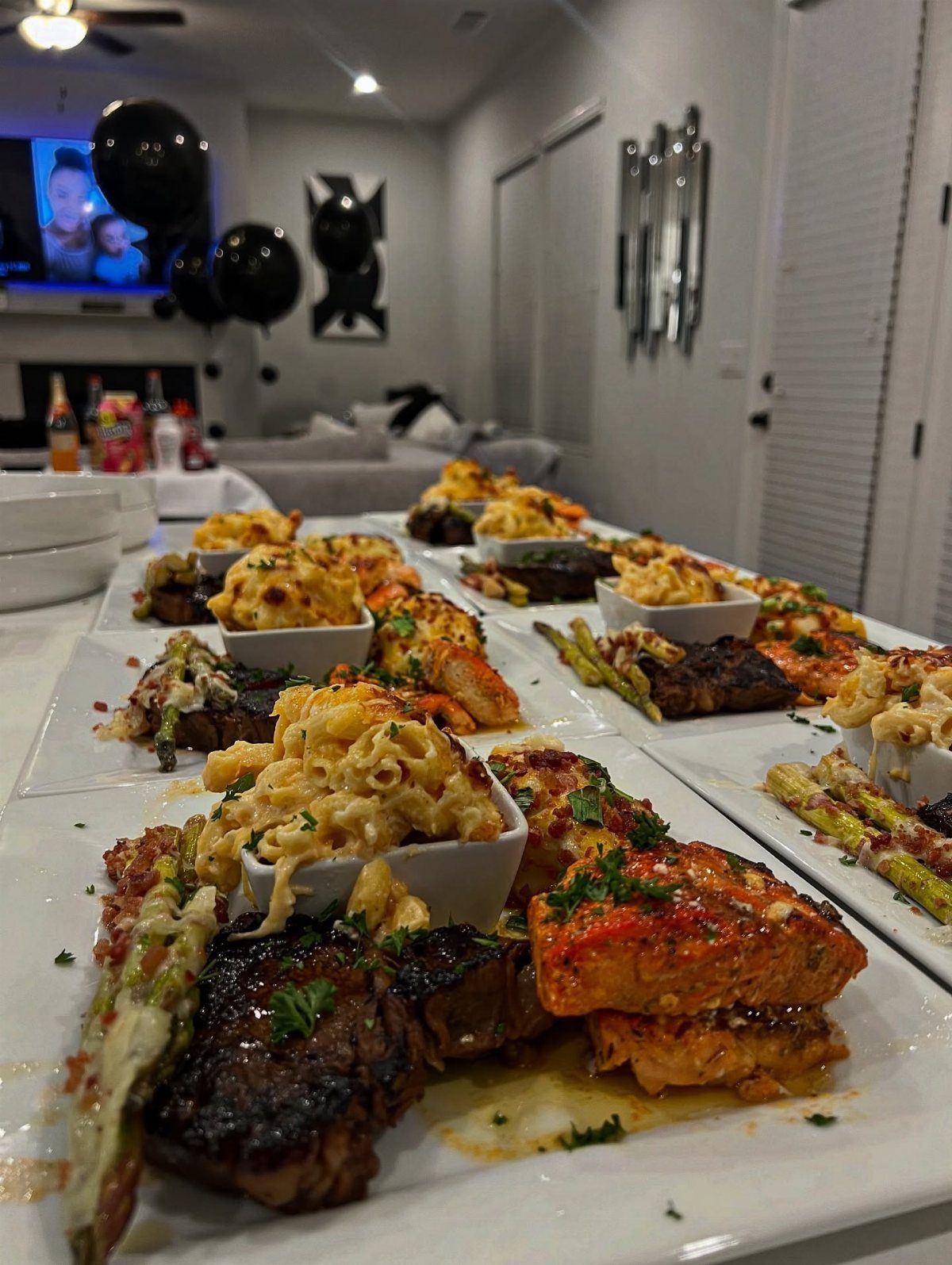 Plates of steak, salmon, and mac and cheese on a long white table.