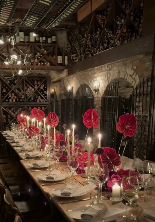 Formal dining table with red flowers and candles inside a stone wine cellar
