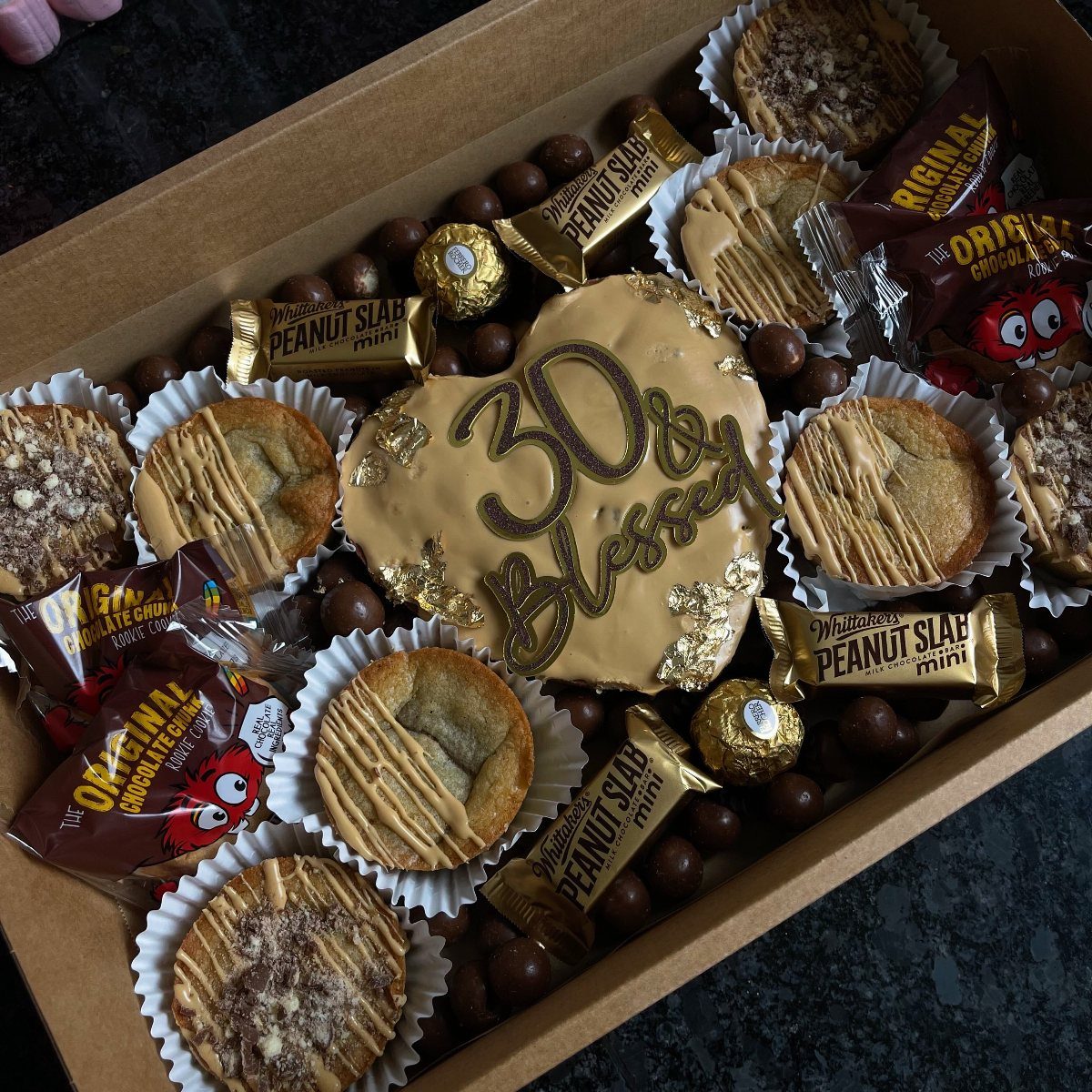 Assorted sweets and cakes in a box with a 30 and Blessed cookie.