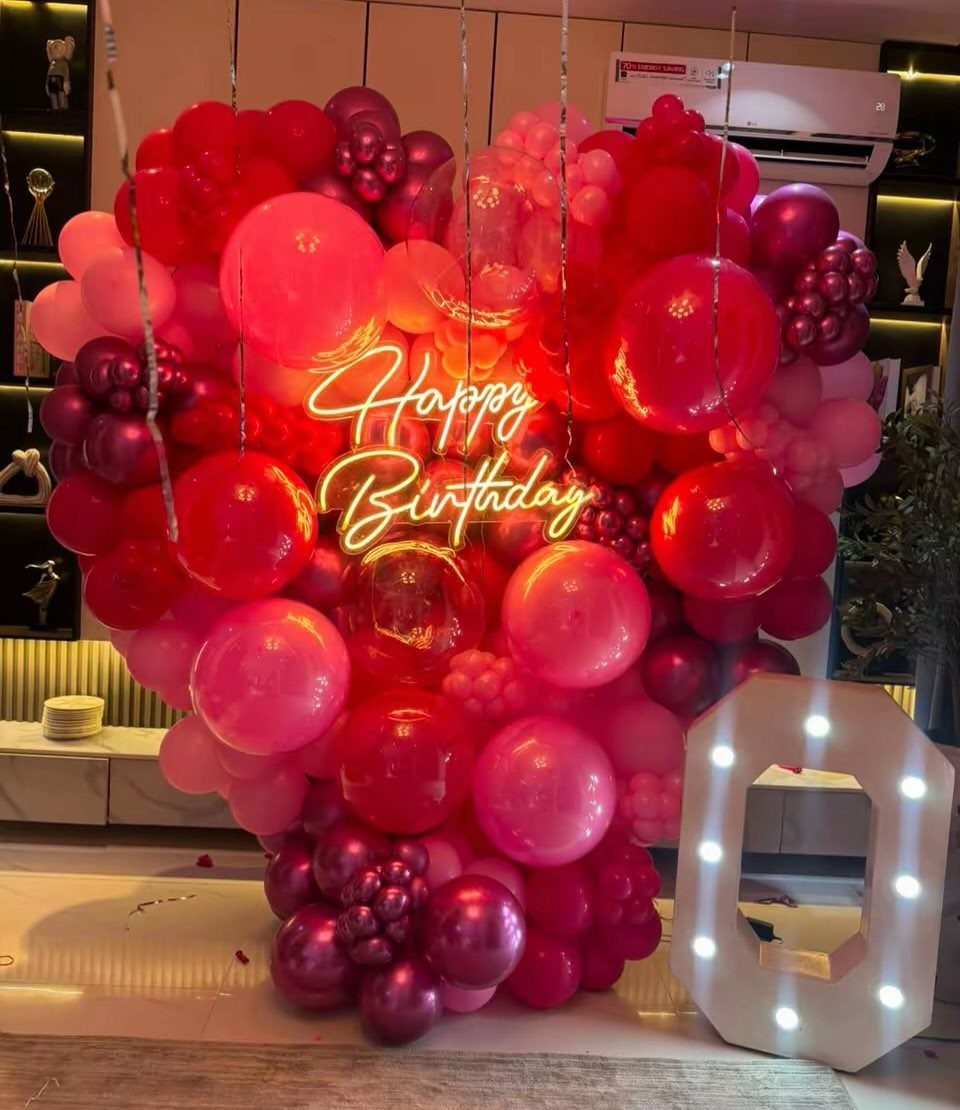 Heart-shaped red and pink balloon arrangement with a Happy Birthday neon sign.