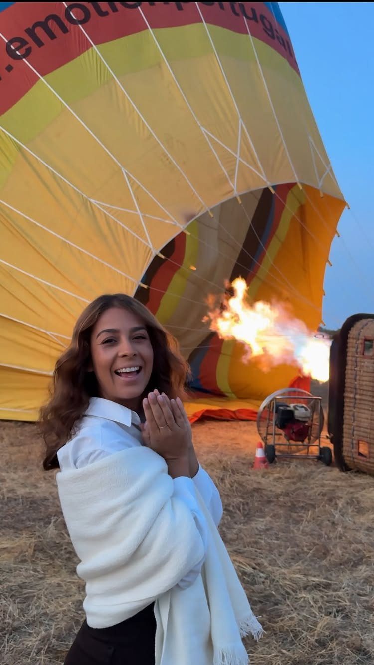 Smiling woman posing in front of a colorful hot air balloon being inflated.