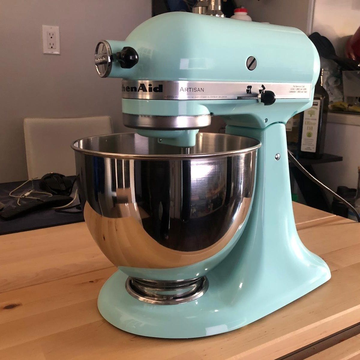 Light blue KitchenAid Artisan stand mixer with stainless steel bowl on wooden counter