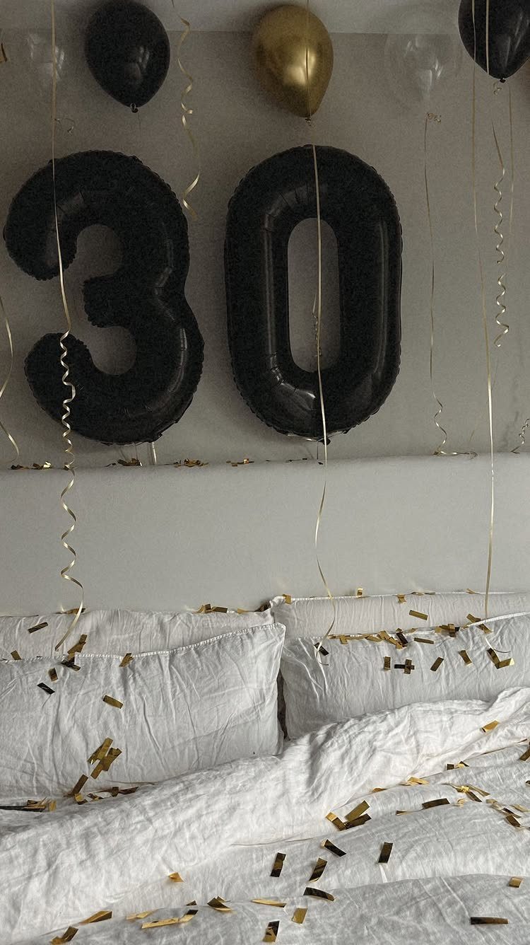 White bed with gold confetti and black number 30 balloons on the wall