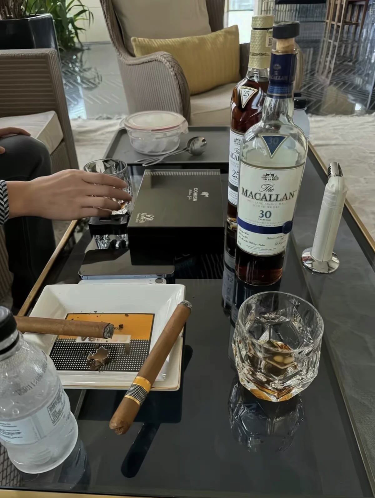 Macallan 30 whiskey bottle and cigars on a black glass coffee table