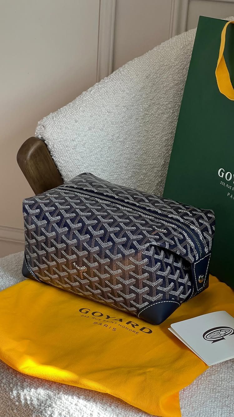 Blue patterned Goyard dopp kit on yellow cloth with green shopping bag.