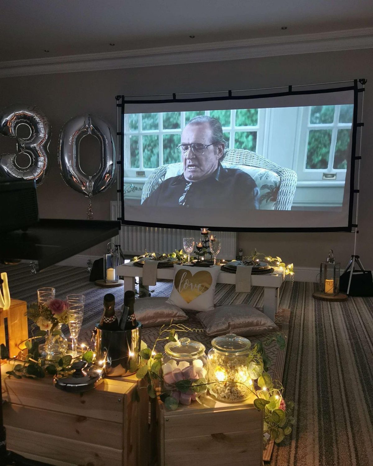 Home cinema setup with 30th birthday balloons, projector screen, and champagne snacks.