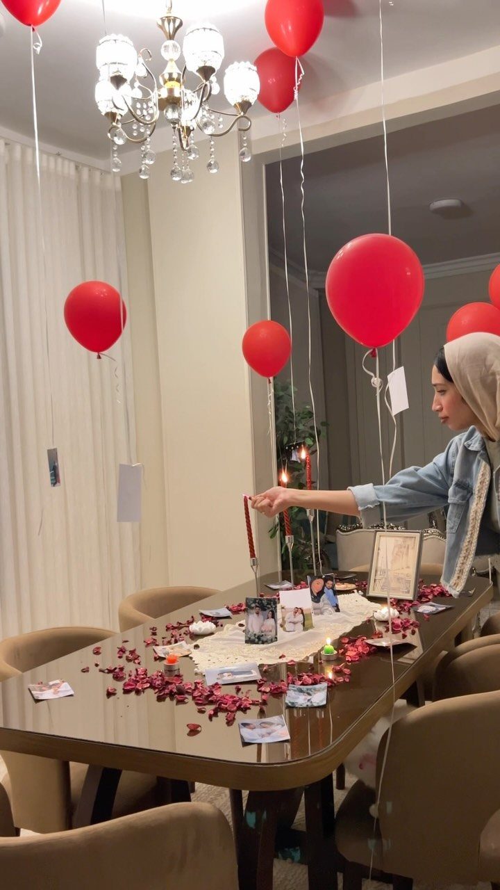Woman arranging a romantic birthday table setup with red balloons and rose petals.