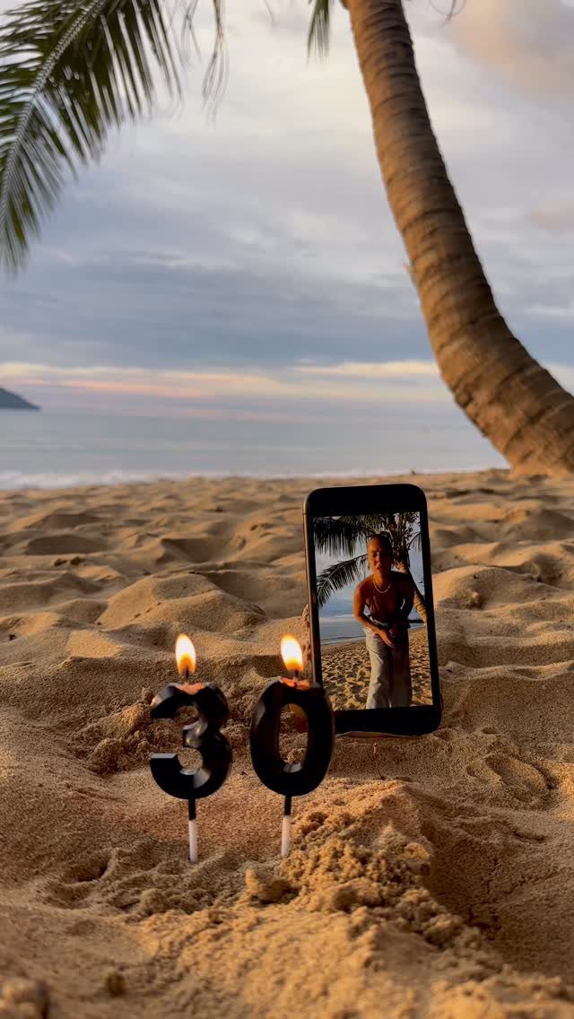 Lit number 30 candles and a smartphone on a tropical sandy beach