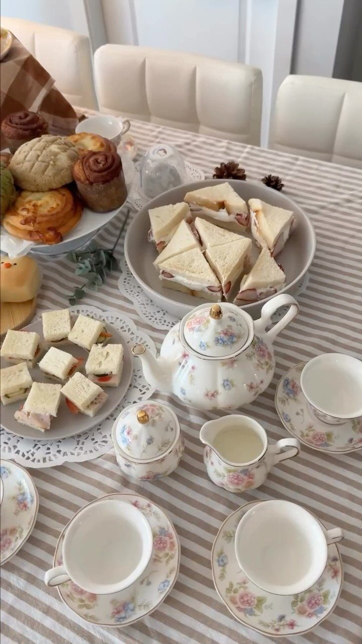 Tea party spread with floral porcelain, triangle sandwiches, and assorted pastries on striped tablecloth