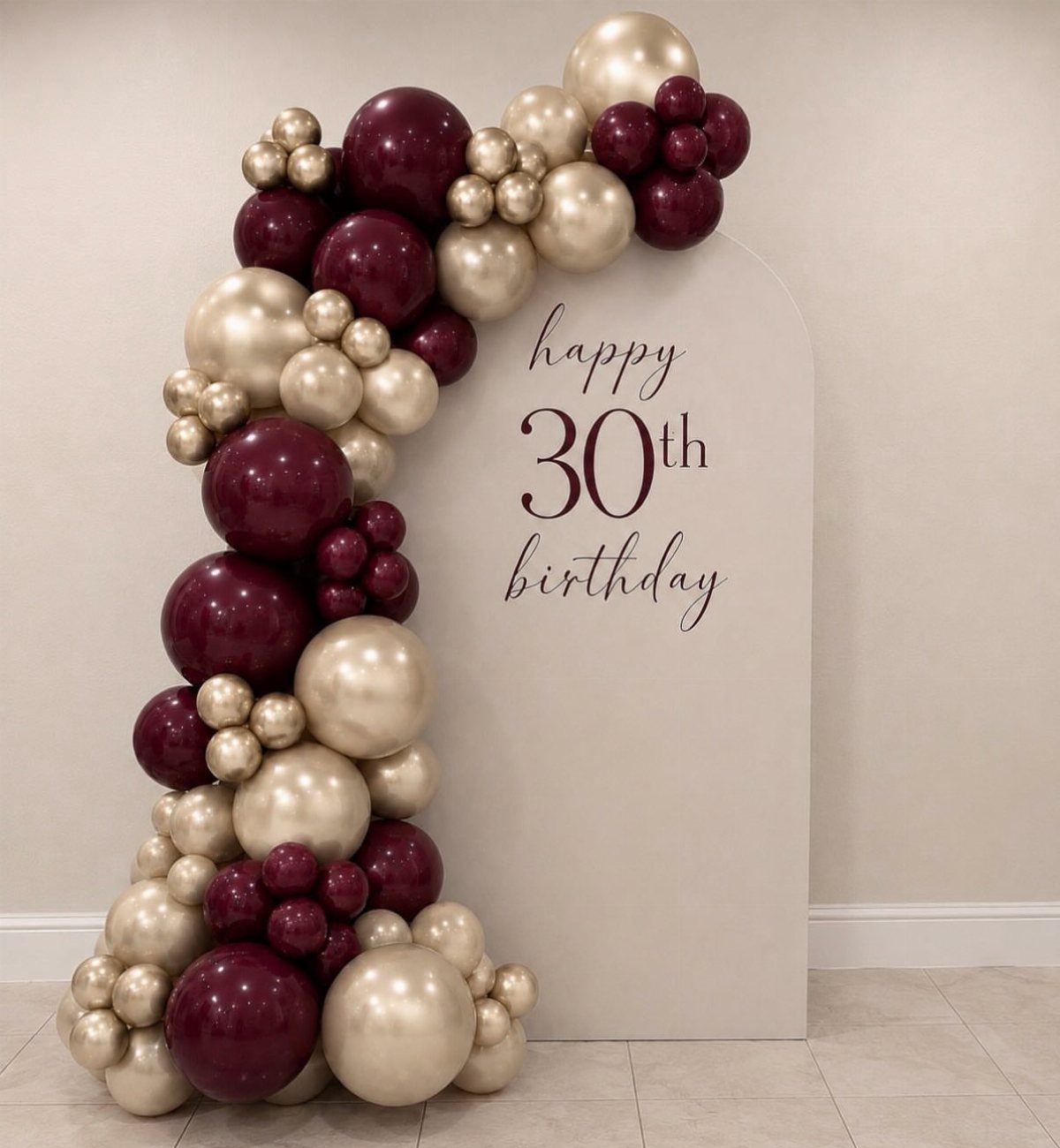 Beige arched birthday backdrop with burgundy and gold balloon garland and 30th birthday text