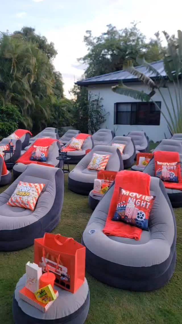 Inflatable lounge chairs with movie-themed pillows and red blankets on a grassy lawn.