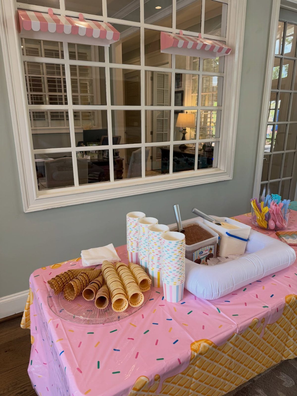 Ice cream station with waffle cones and tubs of ice cream on pink tablecloth