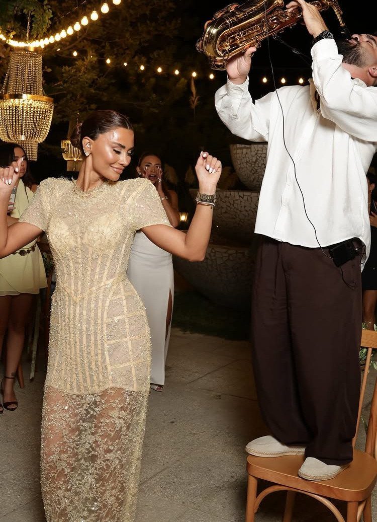 Woman in gold sequined dress dancing while a man plays saxophone at night