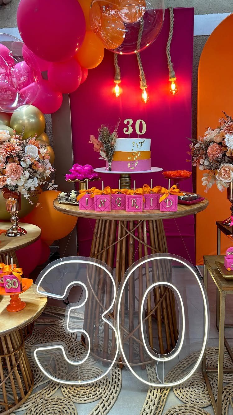 Birthday party decoration with neon 30 sign, cake, and pink and orange balloons.