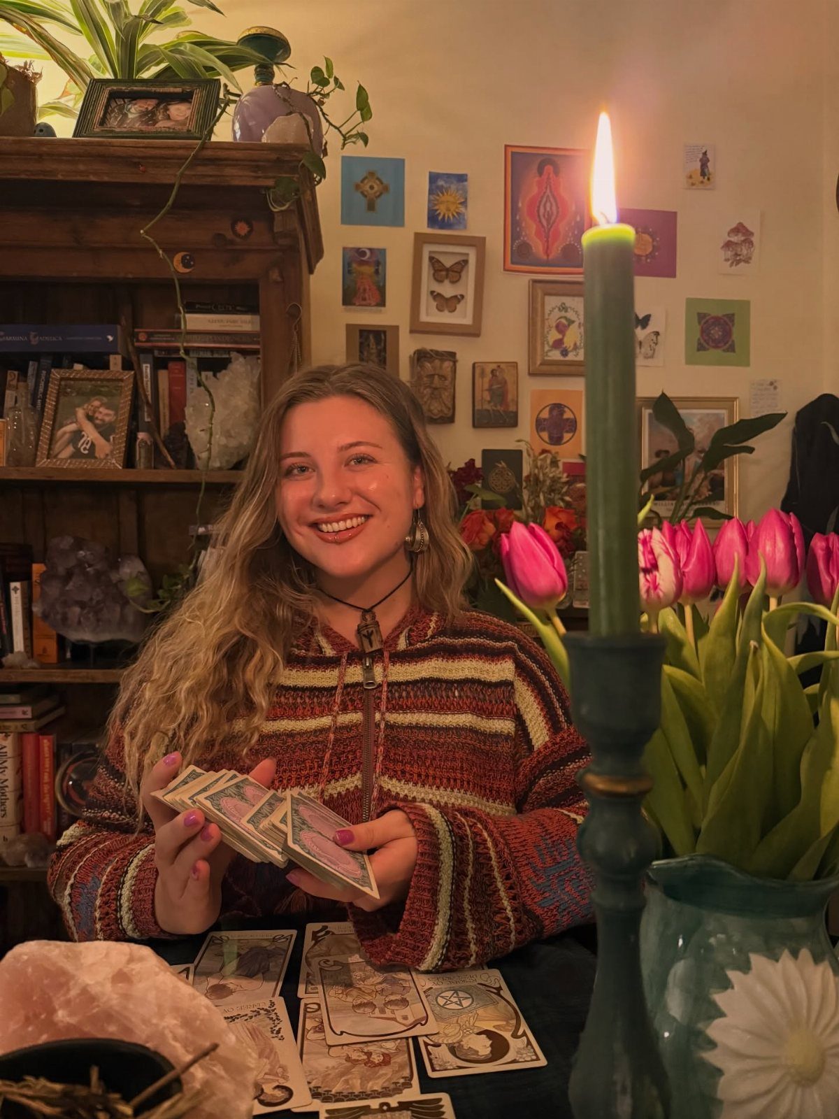 Woman smiling while holding tarot cards at a table with candles and flowers.