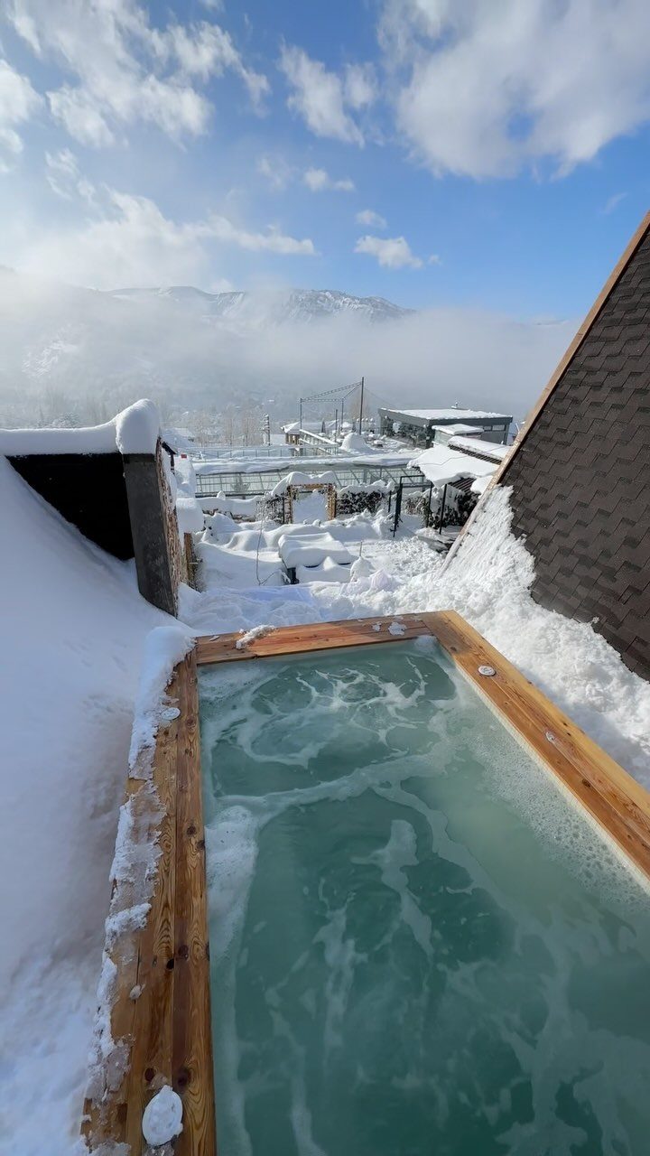 Steaming outdoor hot tub surrounded by snow with a mountain landscape in background