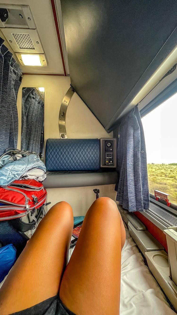 Person's legs resting in a train sleeper cabin with luggage and scenic window view