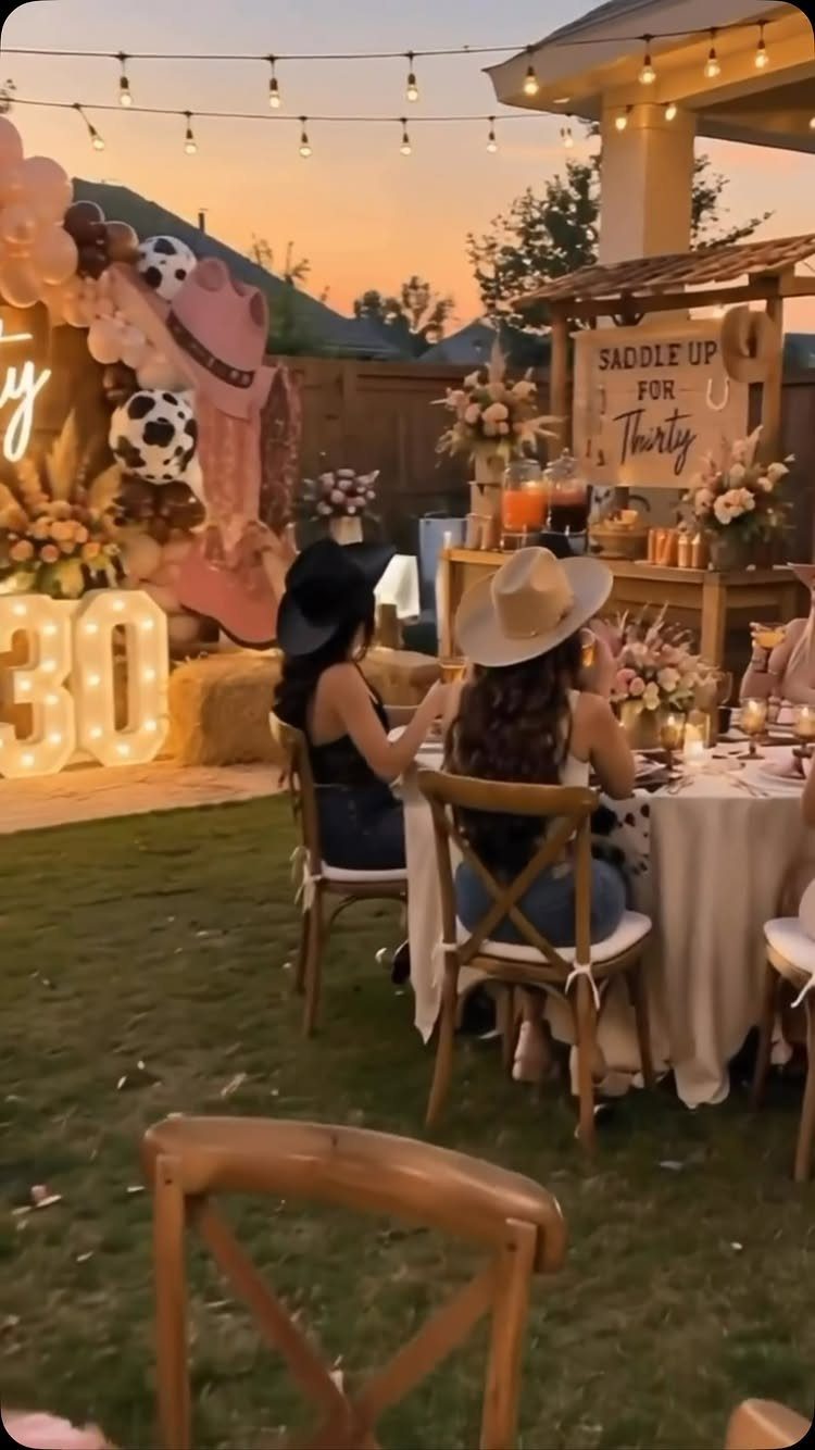 Two women in cowboy hats dining at a 30th birthday party in a backyard.