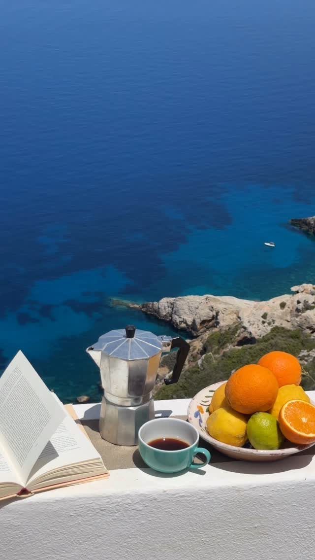 Breakfast setup with coffee and fruit overlooking a rocky Mediterranean coastline and blue sea